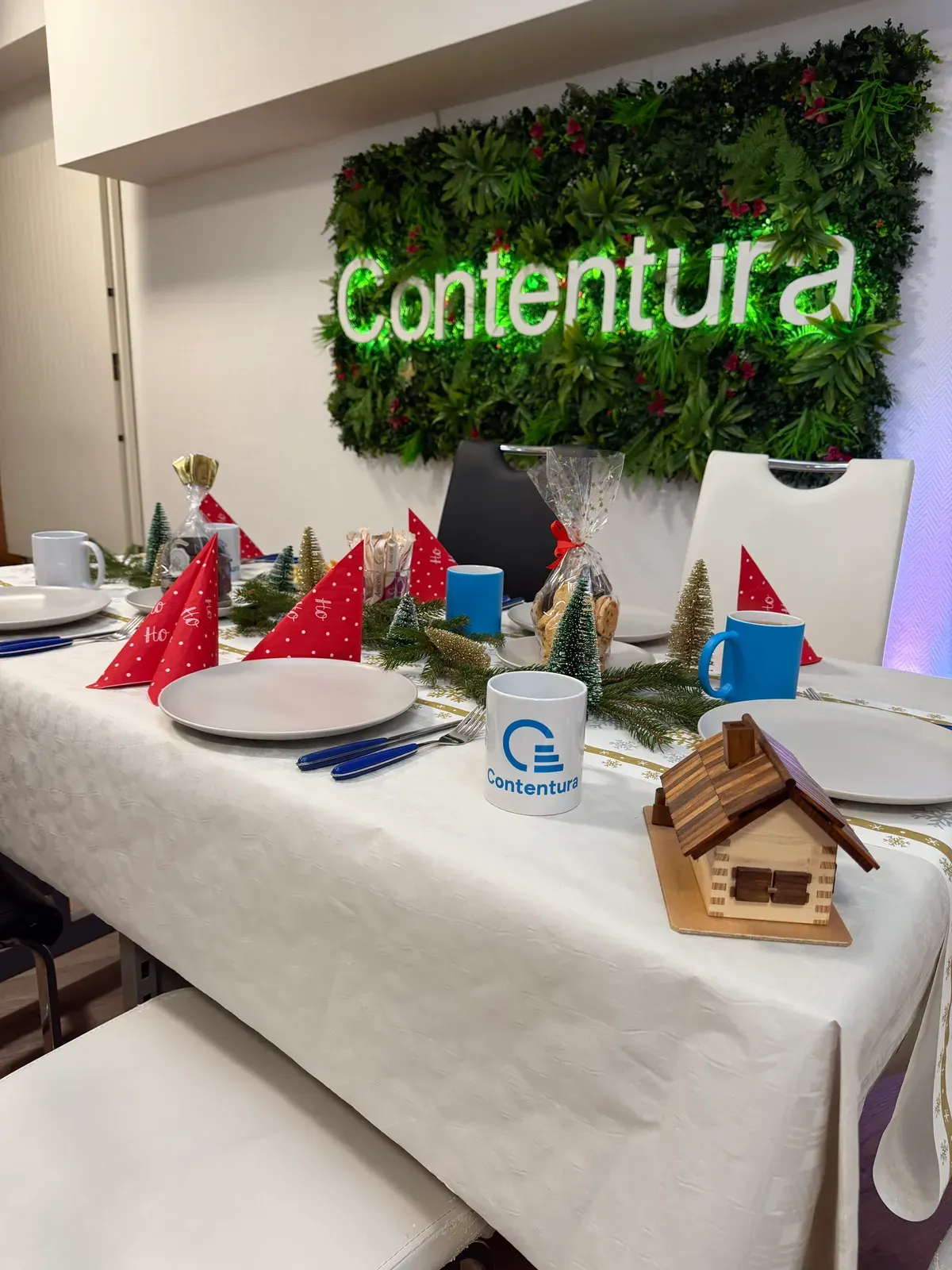 Gedeckte Tafel vor der begrünten Wand mit dem Contentura-Schriftzug, Weihnachtsdeko und Tassen mit Logo